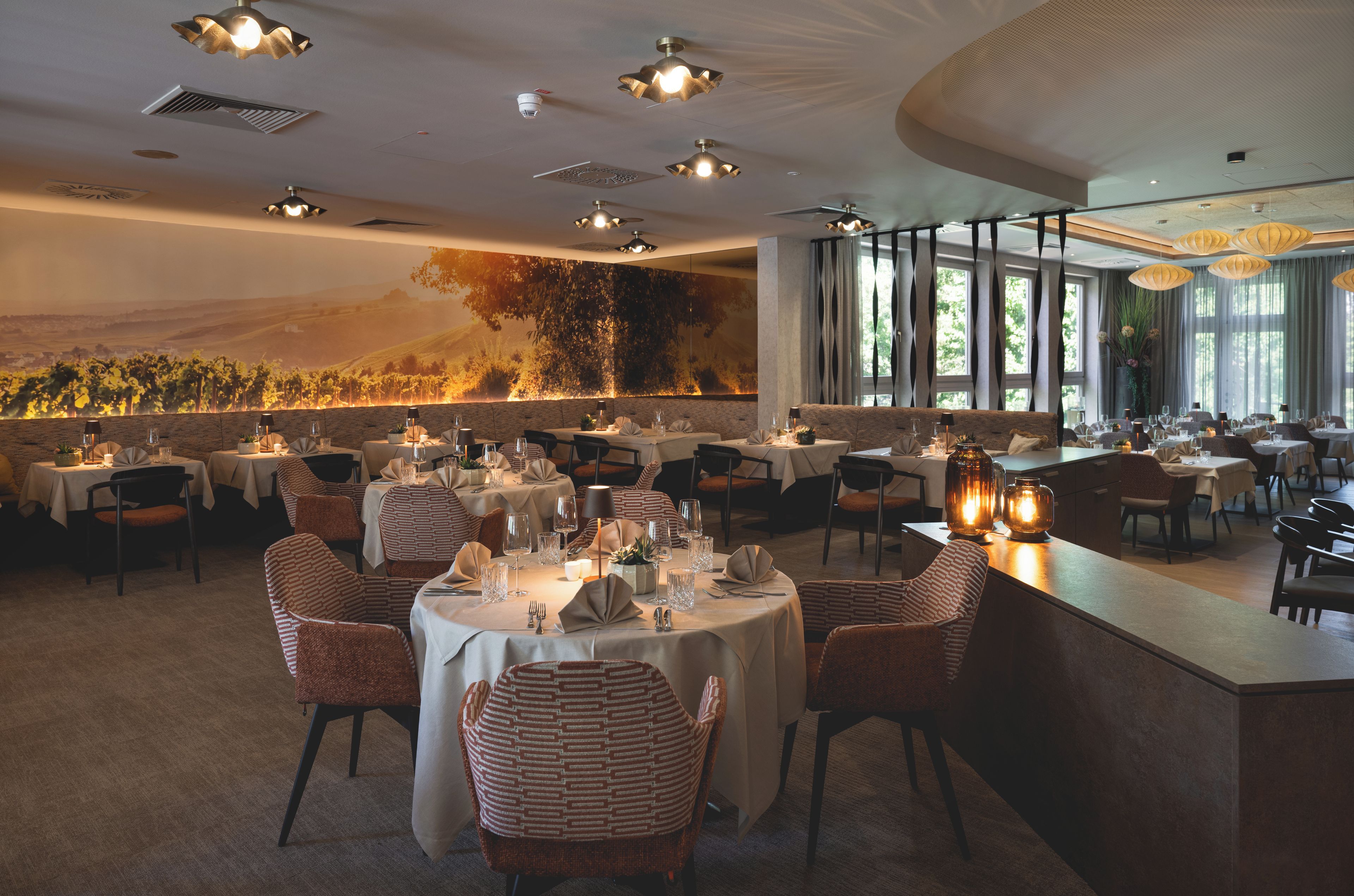 Un restaurant amb taules rodones, cadires i un mural d'una vinya.