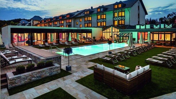 Un hotel con piscina, mobiliario exterior e fachada bien iluminada.