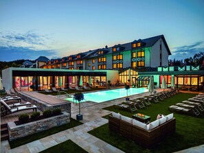 Un hotel con piscina, mobiliario exterior e fachada bien iluminada.