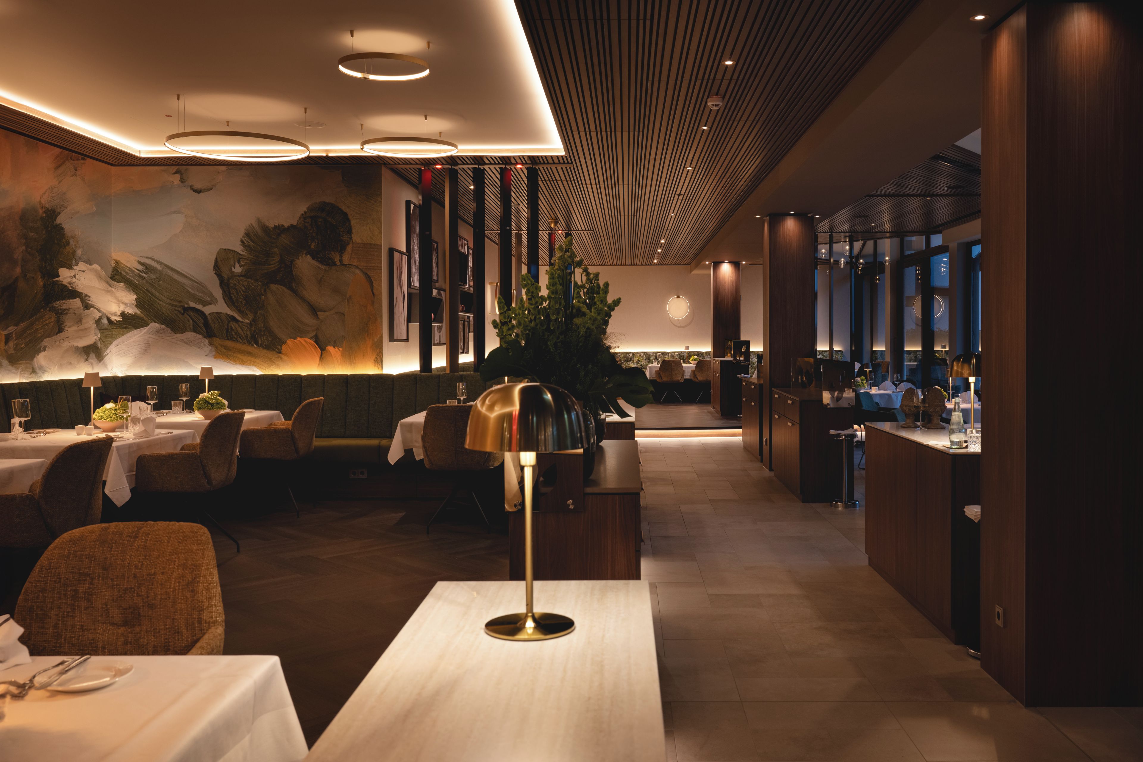 A modern restaurant interior with a dining area, a bar, and a mural on the wall.