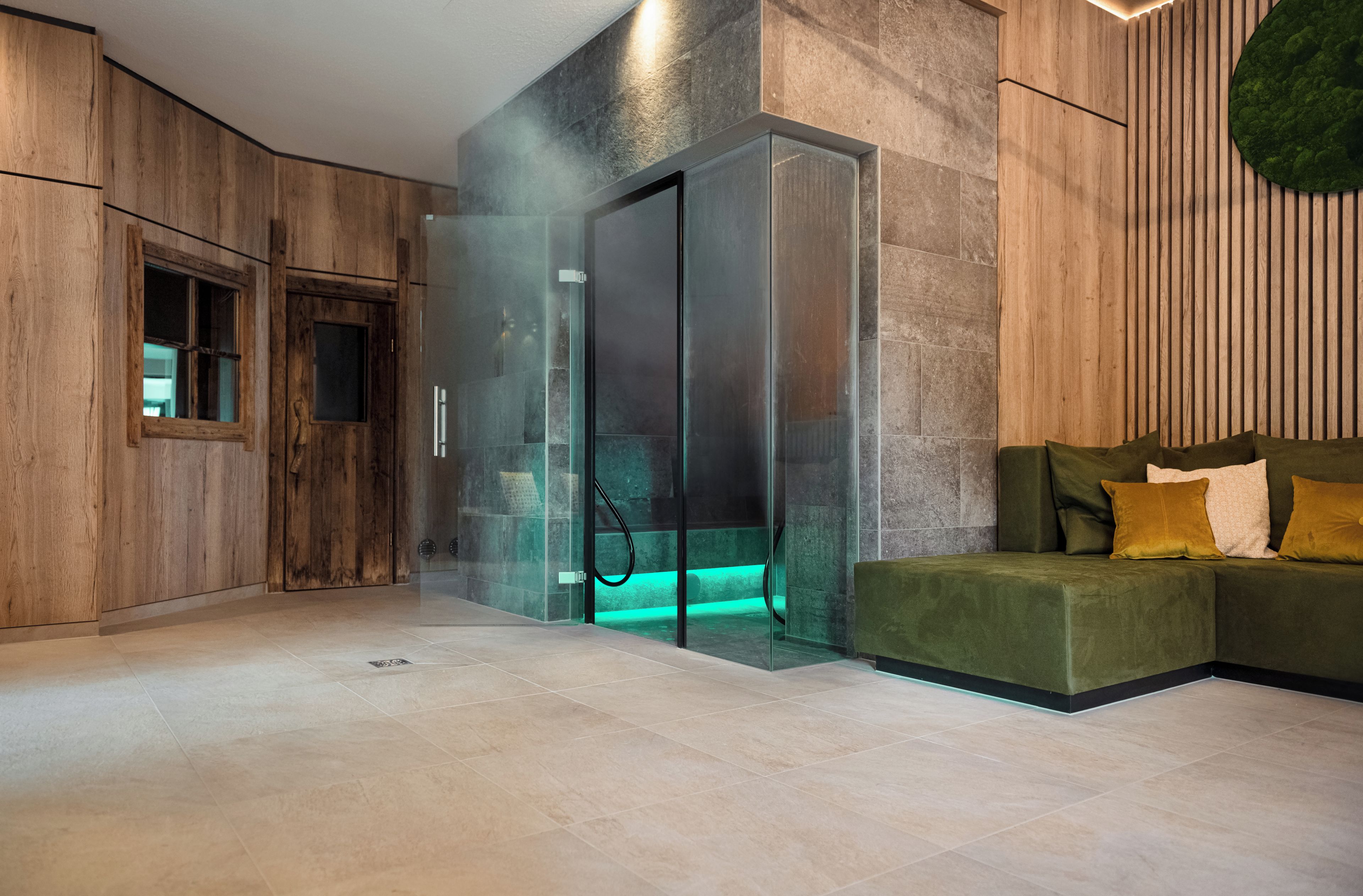 Un intérieur moderne avec un ascenseur en verre, des murs recouverts de panneaux en bois et un canapé vert agrémenté de coussins.