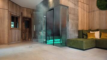 Un intérieur moderne avec un ascenseur en verre, des murs recouverts de panneaux en bois et un canapé vert agrémenté de coussins.