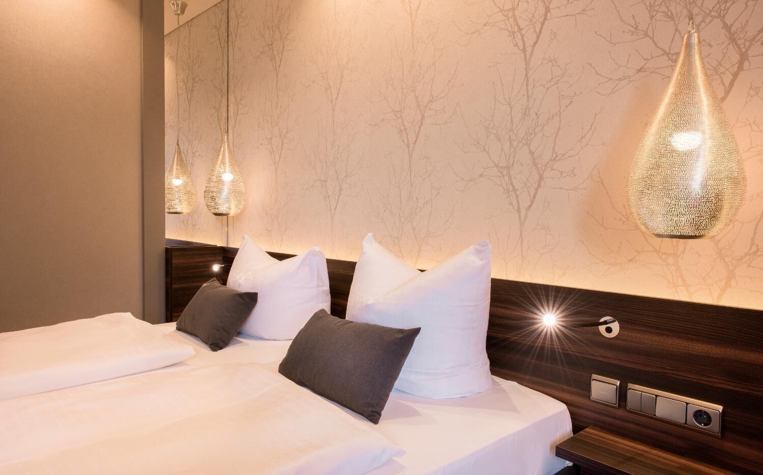 Una habitación de hotel con una cama grande, dos mesitas de noche y una lámpara fijada a la pared.