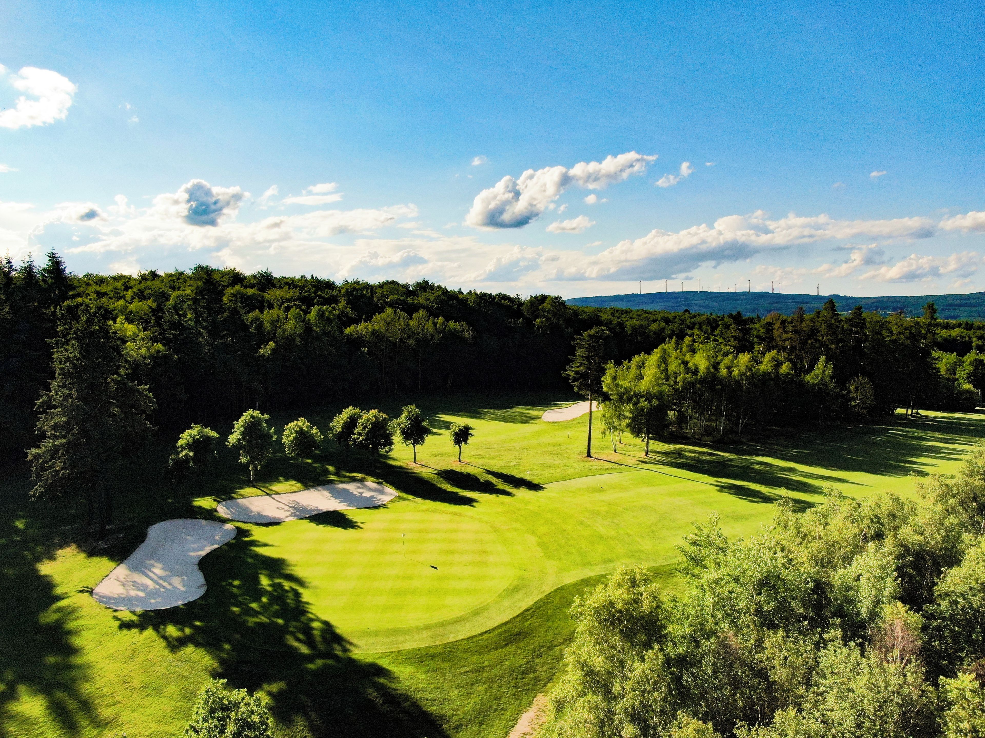 A golf course with sand bunkers, trees, and a clear sky.