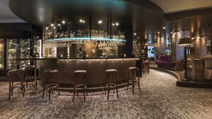 Zona de bar con una barra curva, varios taburetes y una alfombra estampada.