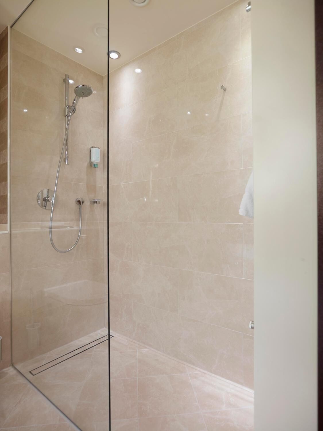 A modern bathroom with a glass shower enclosure, beige tiles, and a visible towel rack.