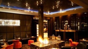 Un espacio lounge moderno con una chimenea central, asientos cómodos e iluminación ambiental.
