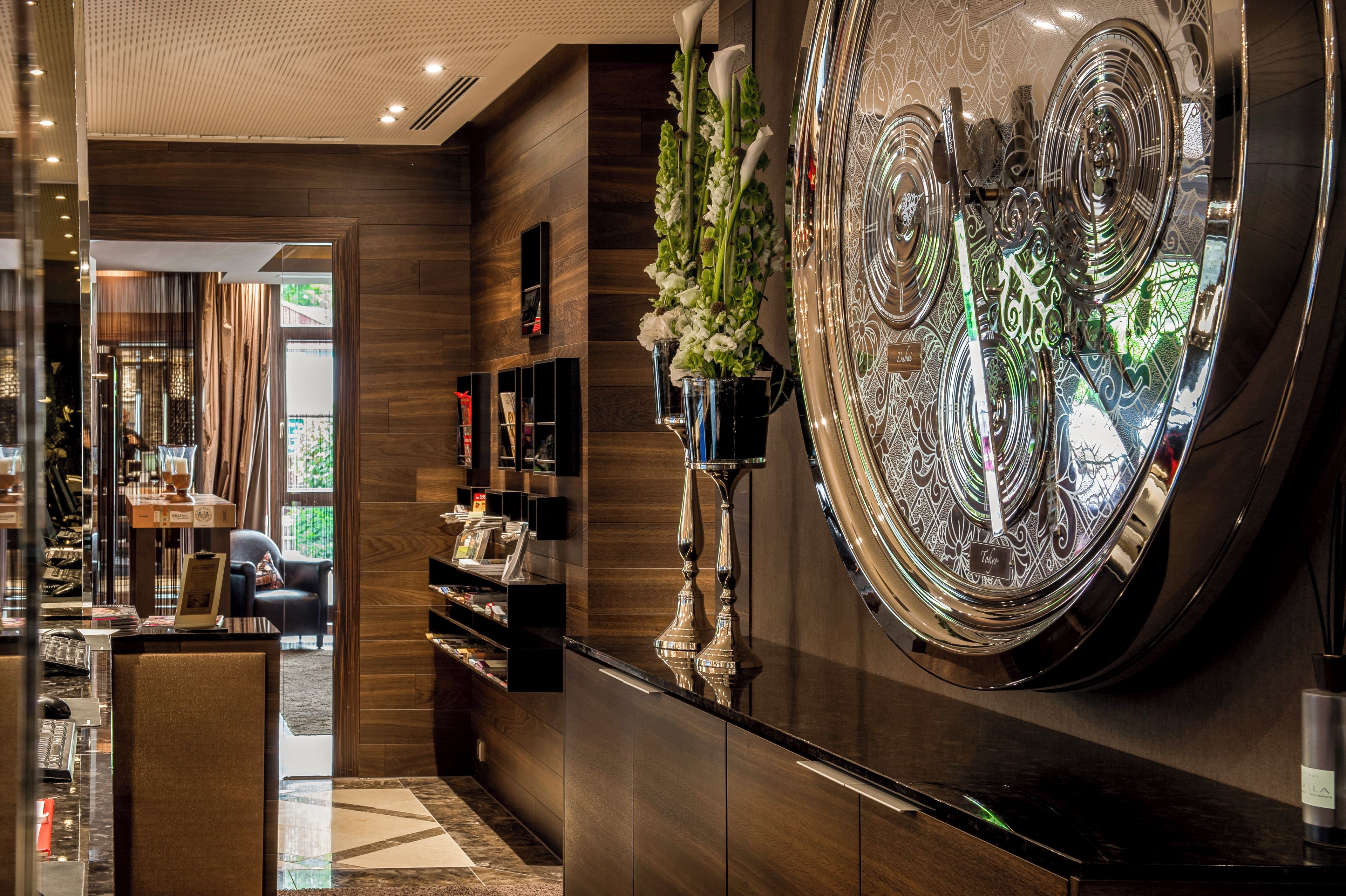 Un hall d’hôtel moderne, doté d’un grand miroir décoratif, d’un comptoir d’accueil et d’un espace salon.