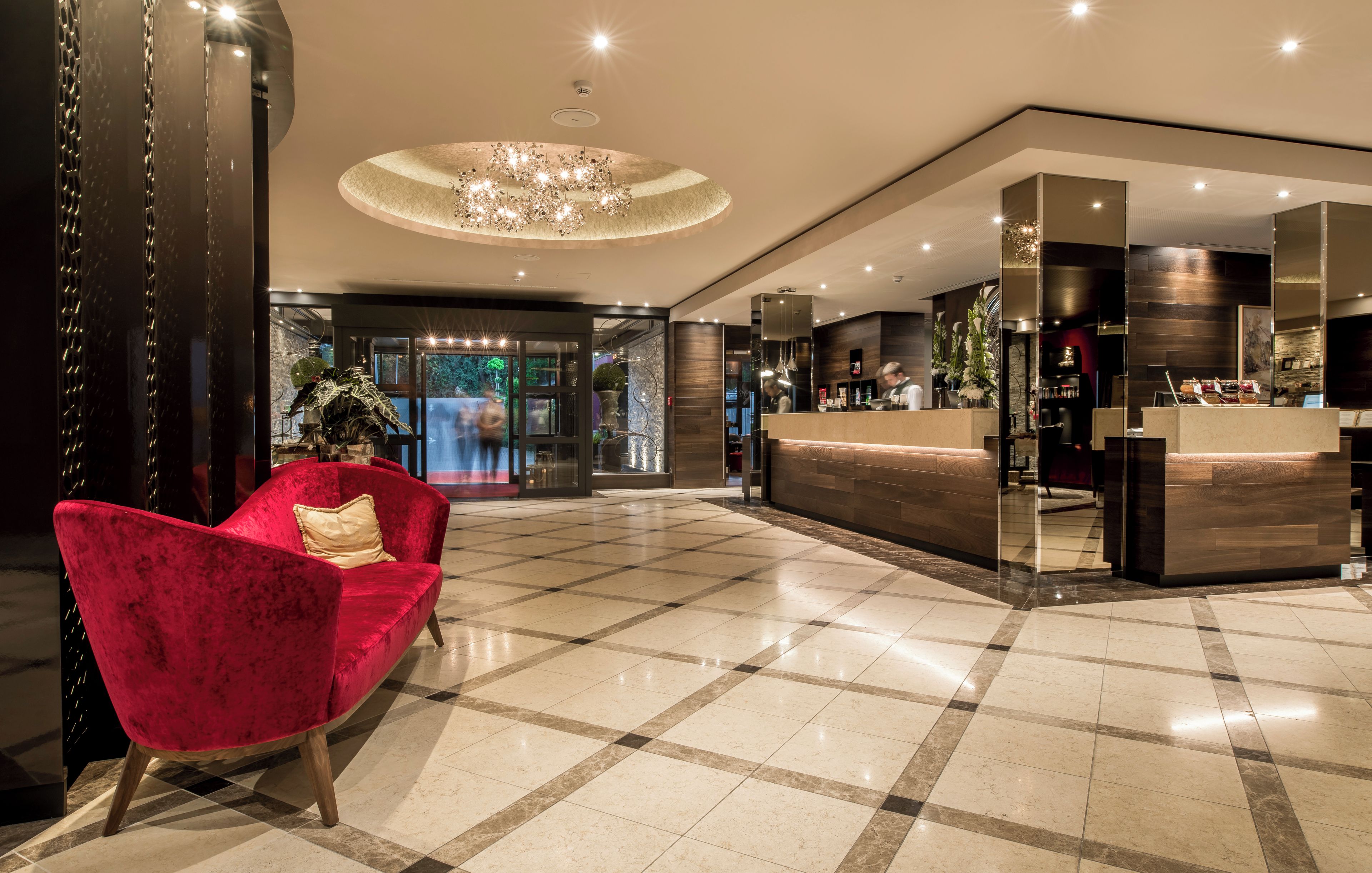 A hotel lobby with a reception desk, a red velvet sofa, and a chandelier.