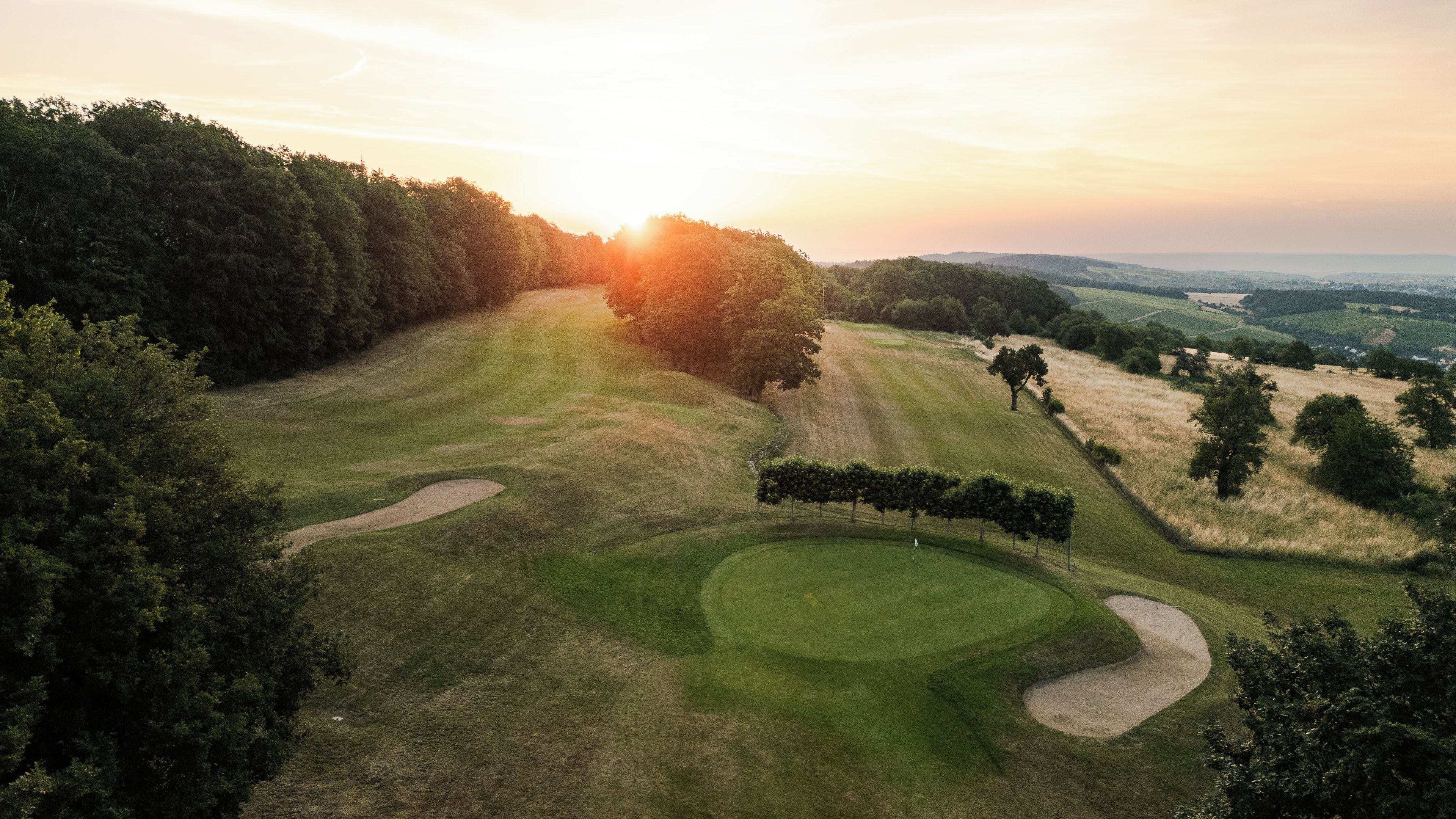 A golf course with sand bunkers, trees, and a clear sky.