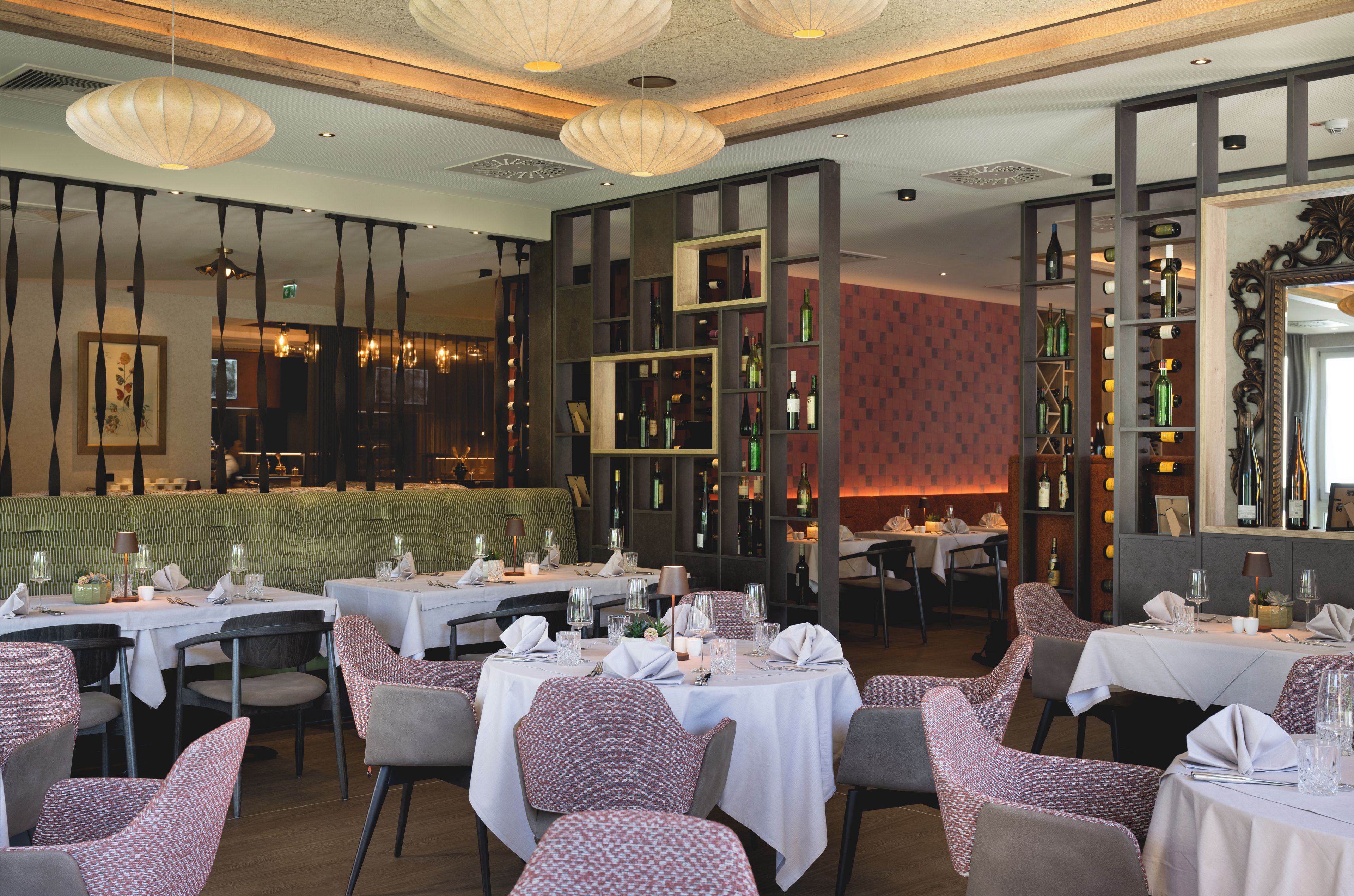 L’intérieur d’un restaurant, avec des tables dressées pour le service, un espace détente avec un banc à motifs et un présentoir à vins.