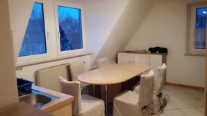 A small kitchen with a dining table and chairs, a radiator, and two windows with blue curtains. - In the house rose garden, center BT. 8 min. , Wifi - free parking, balcony, bus. (Bayreuth)