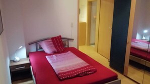 A bedroom with a bed, a bedside table with a lamp, a mirror, and a wardrobe. - In the house rose garden, center BT. 8 min. , Wifi - free parking, balcony, bus. (Bayreuth)