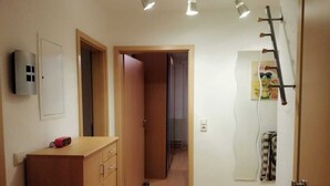 A hallway with a wooden cabinet, a door with a towel hanging, and a wall-mounted light fixture. - In the house rose garden, center BT. 8 min. , Wifi - free parking, balcony, bus. (Bayreuth)