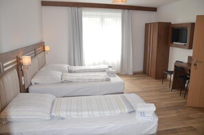 A hotel room with two beds, a desk, a TV, and a window with curtains.