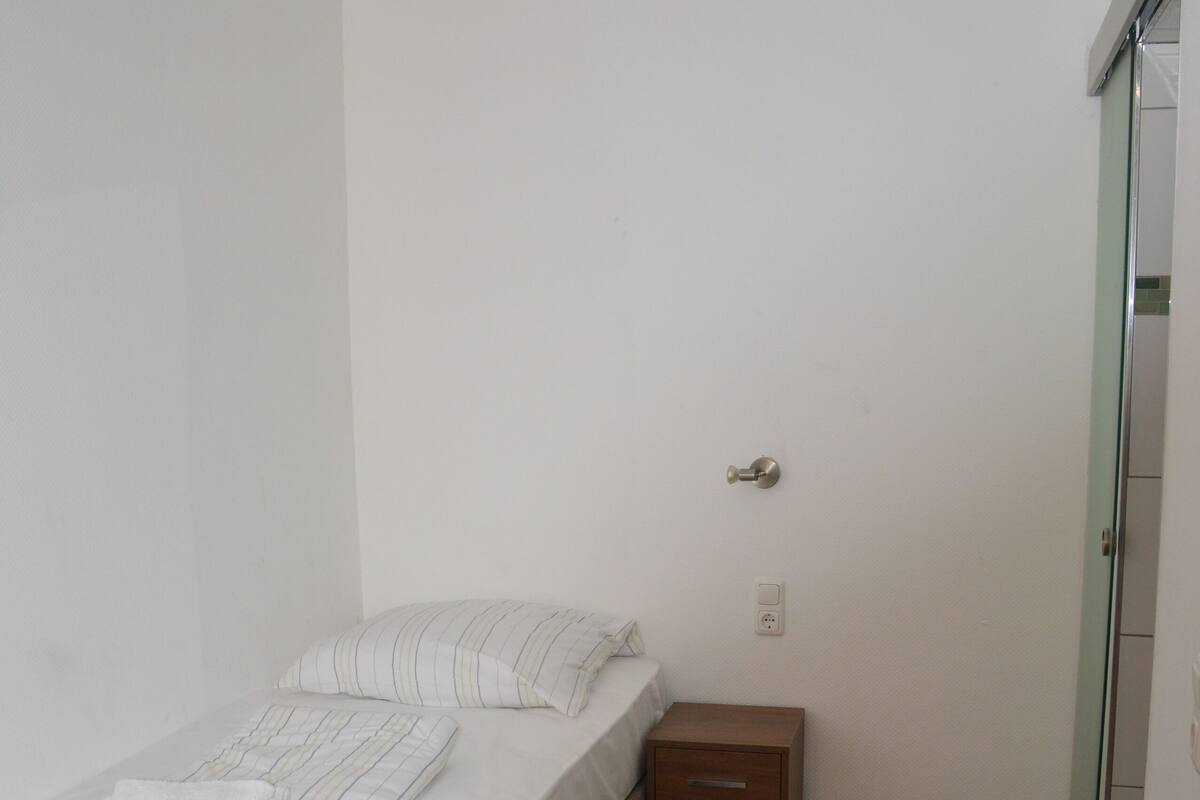 A small, clean room with a single bed, a bedside table, and a wardrobe.
