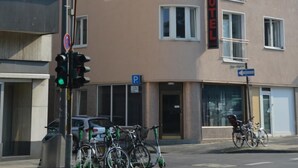 Ein Hotel mit einem Schild, das es als solches kennzeichnet. Vor der Tür stehen Fahrräder, ein Ampelsignal und ein Parkplatzschild.