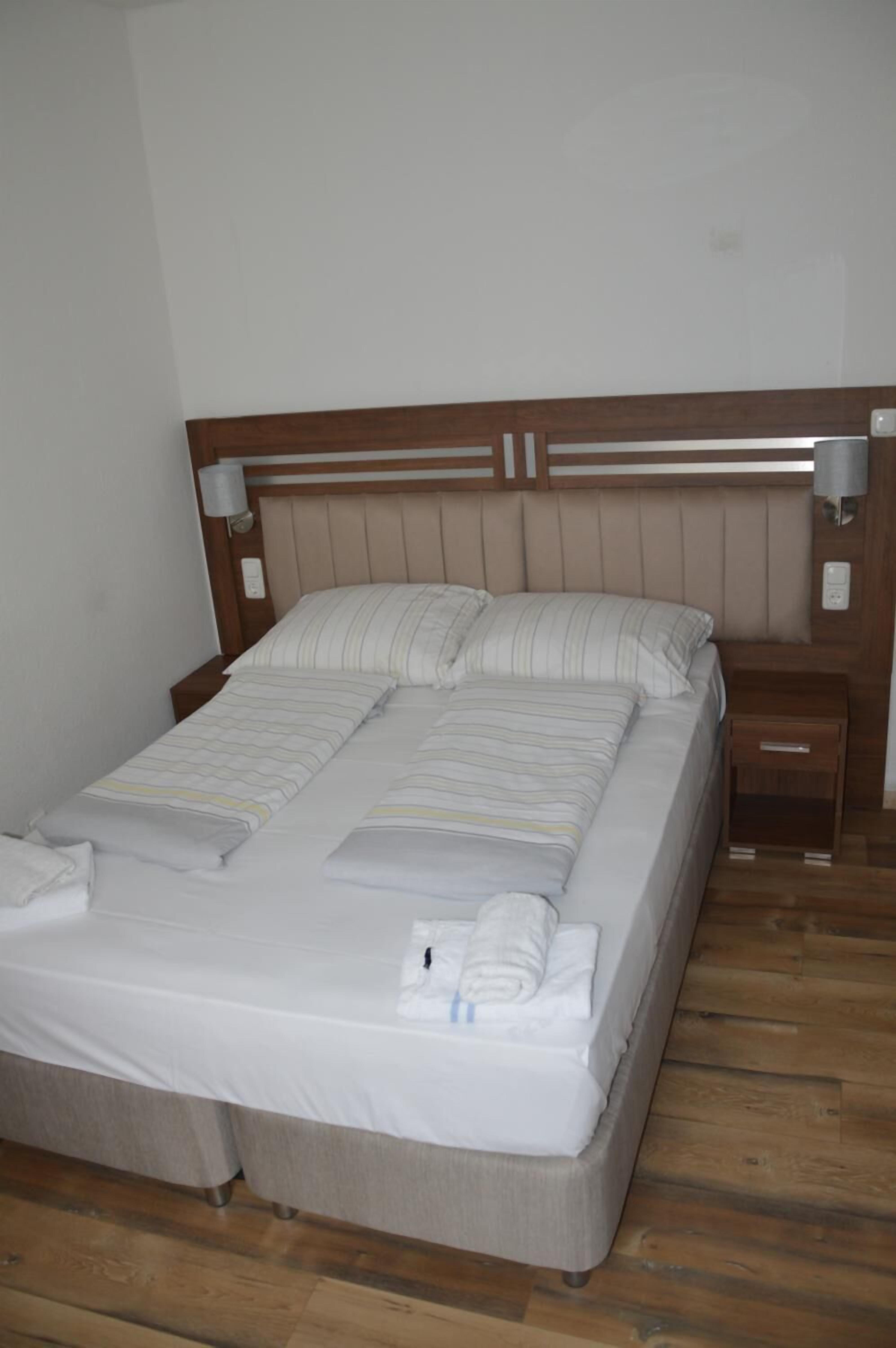 A neatly made bed with a wooden headboard, a bedside table, and a wall-mounted lamp.
