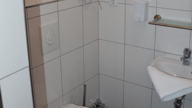 A small, tiled bathroom with a toilet, sink, and a mirror. - Hotel Colonia (Cologne)