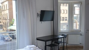 A hotel room with a bed, a desk, a chair, a TV, and a window with a view of the street. - Hotel Colonia (Cologne)