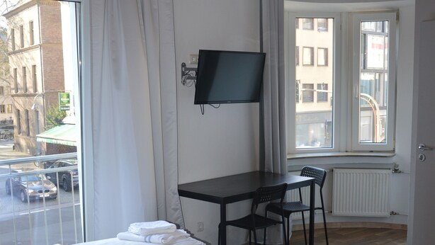 Ein Hotelzimmer mit Bett, Schreibtisch, Stuhl, Fernseher und Fenster mit Blick auf die Straße.