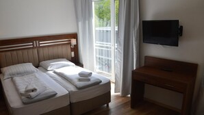 Ein Hotelzimmer mit zwei Betten, einem Holztisch, einem Fernseher und einem Balkon mit Vorhängen.