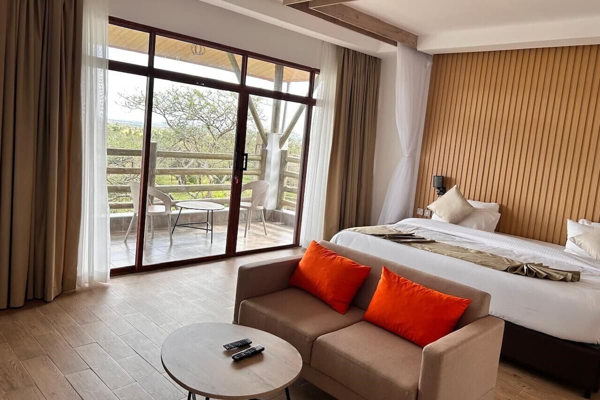 A hotel room with a bed, a sofa, a small table, and a sliding glass door leading to an outdoor area.