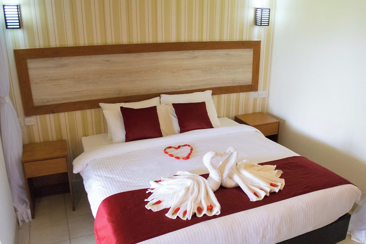 A hotel room with a large bed, striped wallpaper, and a wooden headboard.