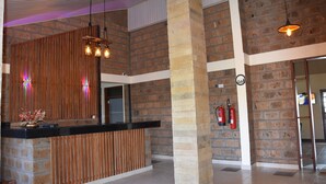 Un espace d’accueil doté d’un comptoir de réception en bois, de murs en briques et de luminaires suspendus.