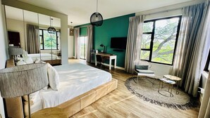 A modern hotel room with a large bed, a desk, a TV, and a balcony with a view of trees. - Little Forest Garden Retreat Guesthouse (Windhoek)
