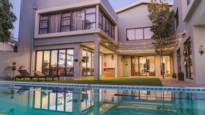 A modern two-story house with a swimming pool, large windows, and string lights. - Little Forest Garden Retreat Guesthouse (Windhoek)