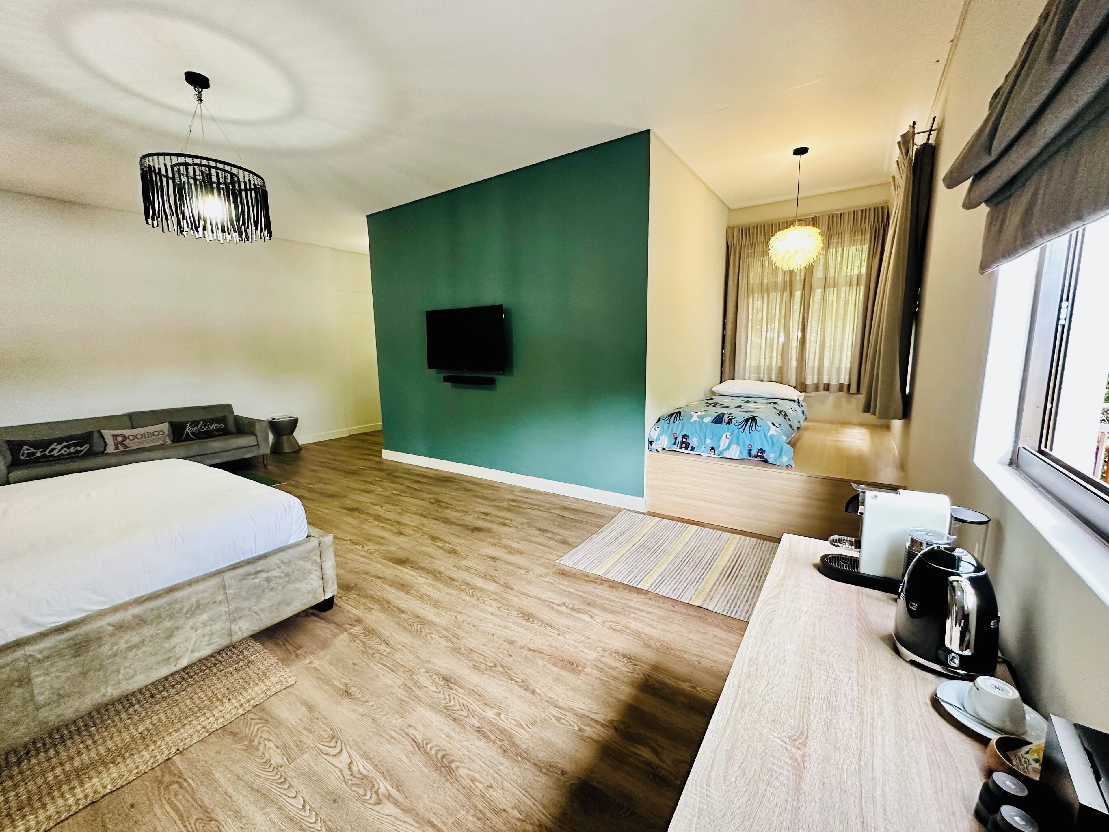 Habitación de hotel con cama, escritorio con hervidor, televisor y ventana con cortinas.
