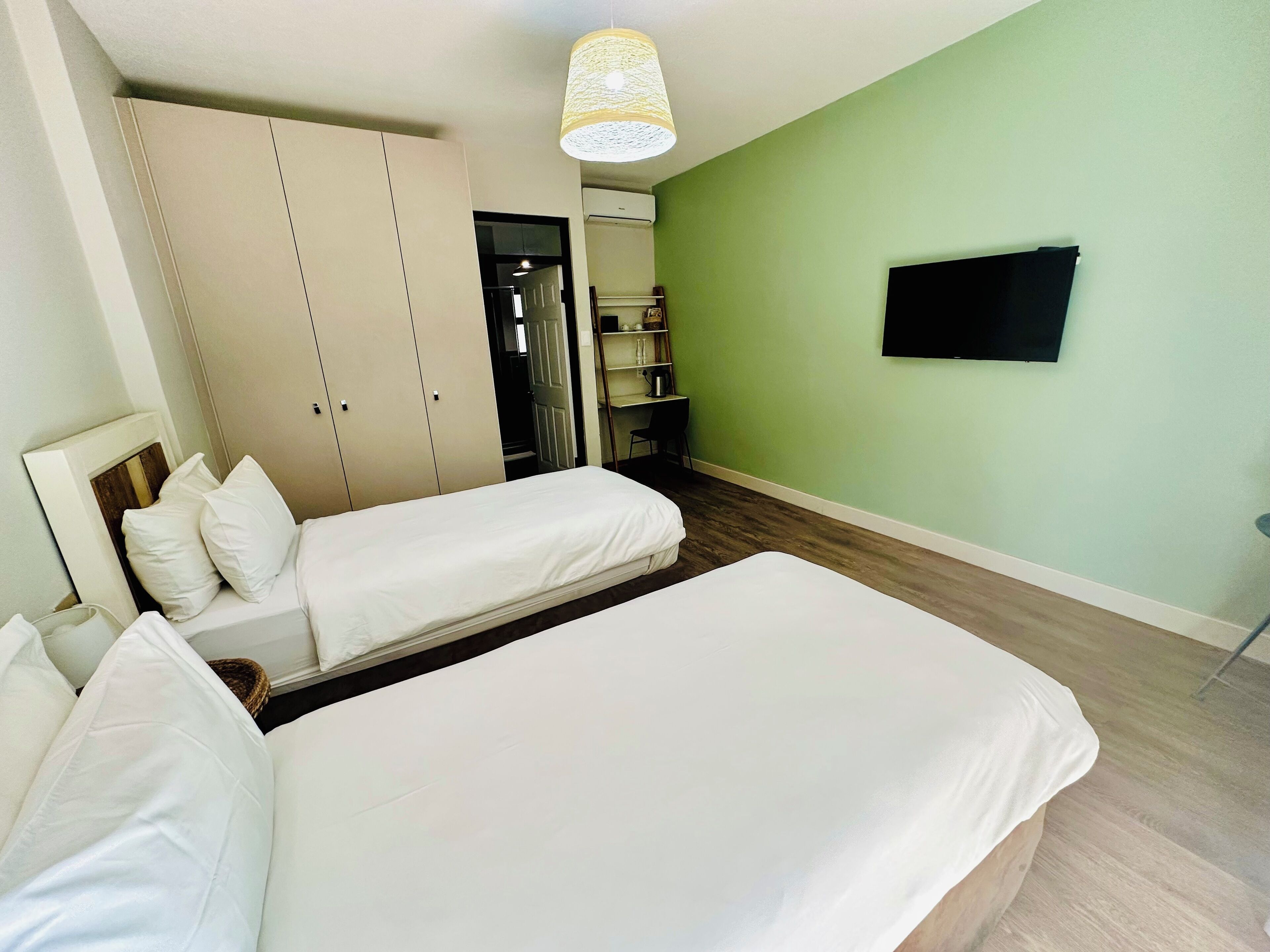 A hotel room with two beds, a wardrobe, a television, and a lamp.