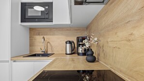 Eine moderne Küche mit integriertem Mikrowellenherd, einer Kaffeemaschine und einem Wasserkocher auf einer Holz Arbeitsplatte.