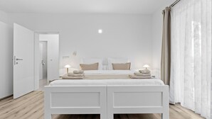 Ein modernes Schlafzimmer mit einem großen Bett, Nachttischlampen und Blick ins Freie durch transparente Vorhänge.