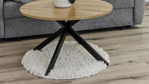 Ein modernes Wohnzimmer mit grauem Sofa, weißen Kissen, einem runden Couchtisch aus Holz und einem weißen Shaggy-Teppich.