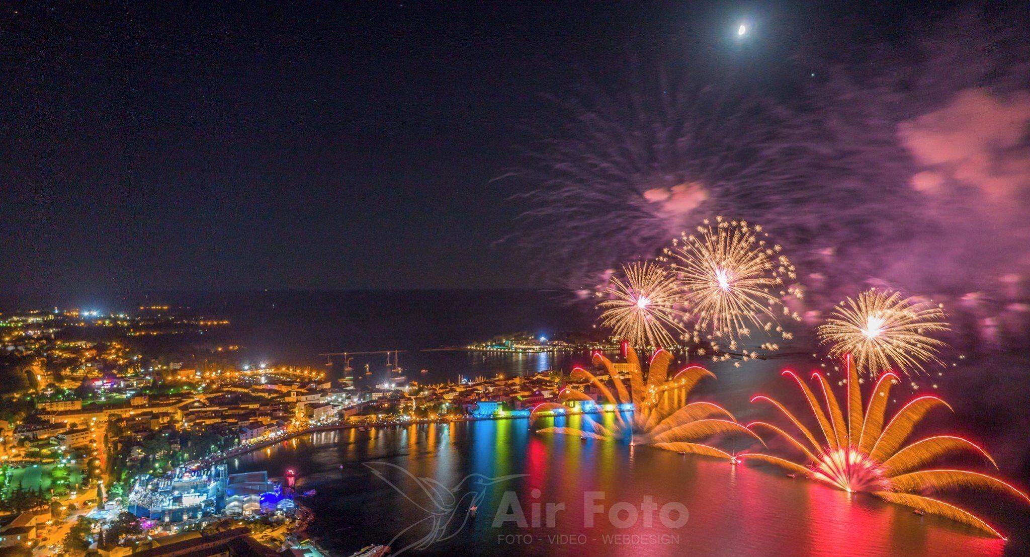 A nighttime cityscape with fireworks over a body of water, city lights, and a clear sky.