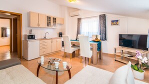 Een modern appartement met keuken, eethoek en woonkamer. Het heeft een flatscreen-tv, een eettafel met stoelen, een salontafel en een bank.