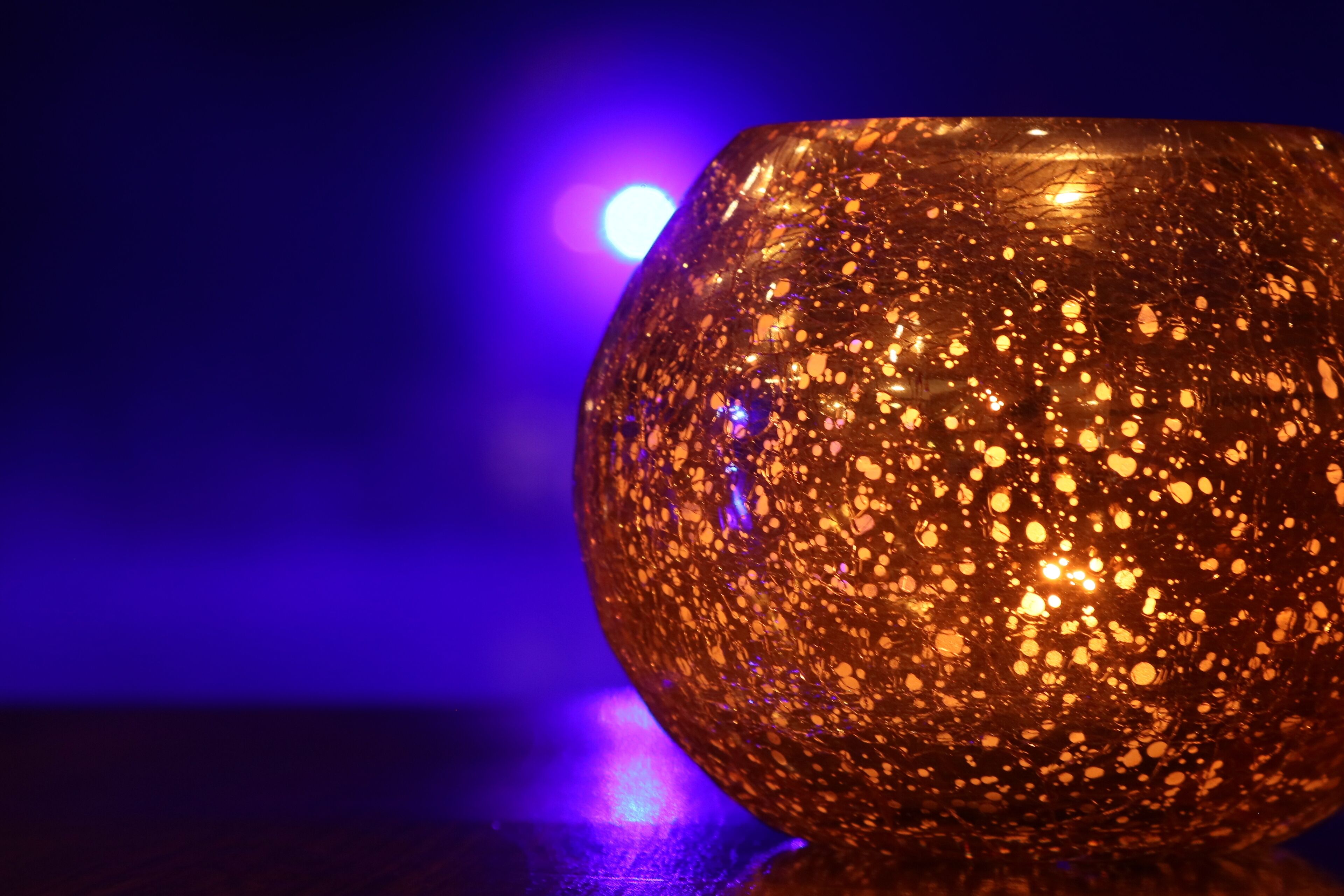 A spherical object with a speckled surface, reflecting light, against a dark background with a blue hue.