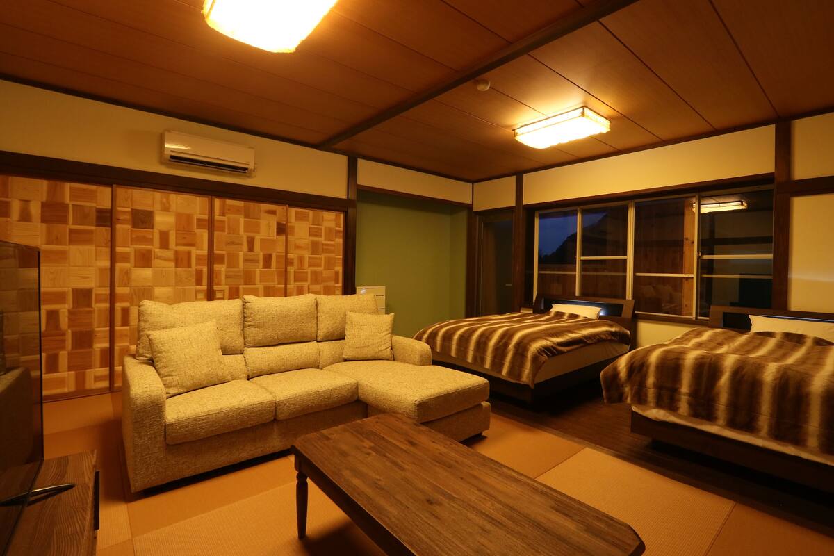 A hotel room with a sofa, two single beds, a wooden table, and a wall with a geometric pattern.