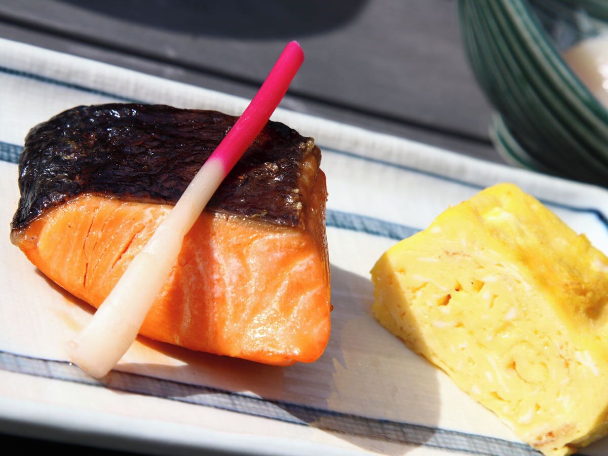 Une assiette contenant un morceau de saumon et une tranche d’un aliment jaune, peut-être un plat à base de pommes de terre, posée sur une nappe à rayures.