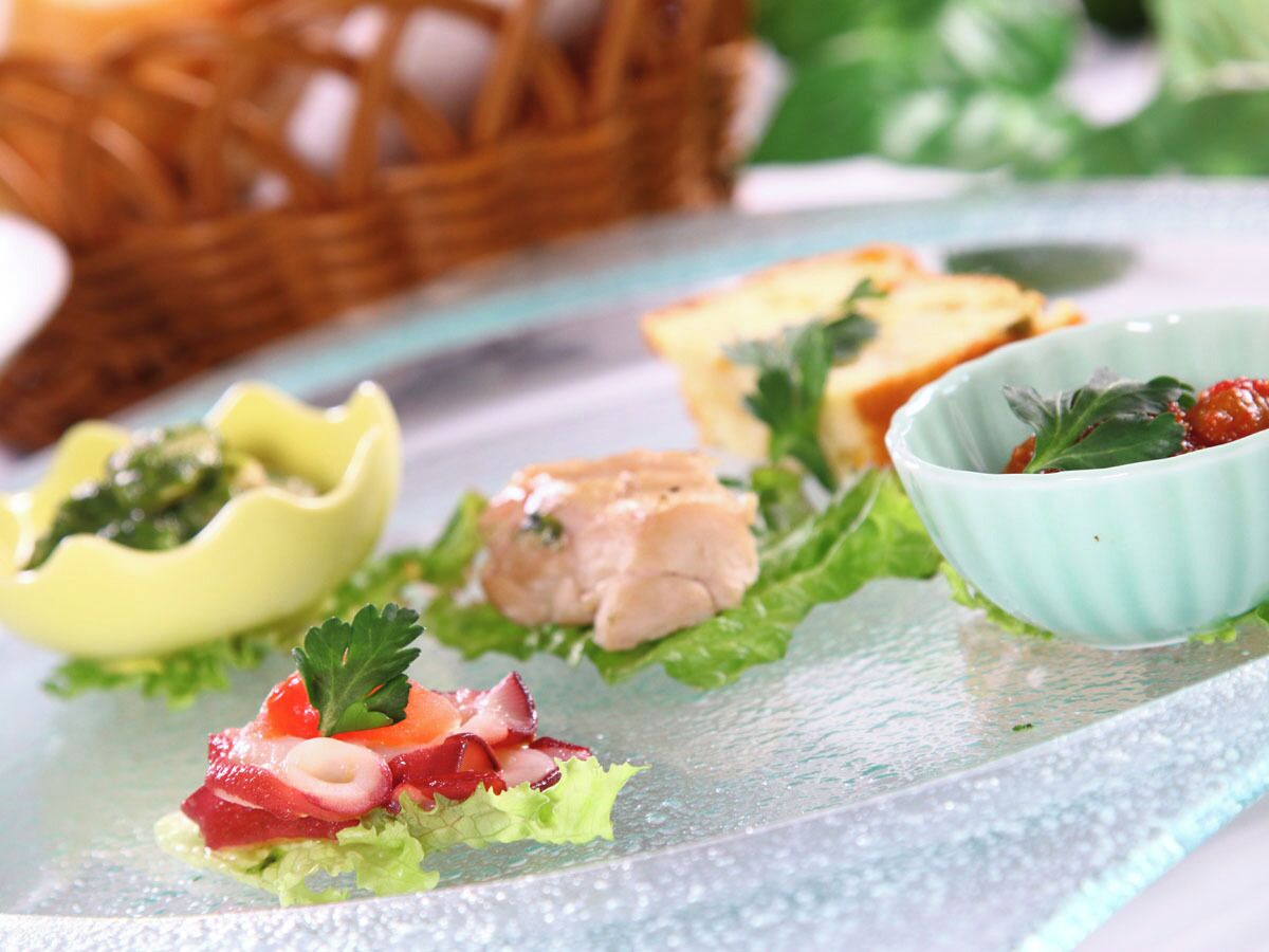 A variety of appetizers on a glass plate, including a yellow bowl with a green topping, a bowl with a red topping, and a bowl with a green topping.