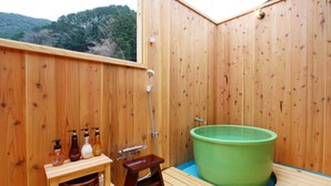 Un spa con paredes de madera, una tina verde grande, estantes de madera con botellas y un taburete pequeño de madera.