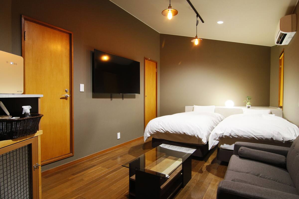 A hotel room with two beds, a flat-screen TV, a wooden cabinet, and a sofa.