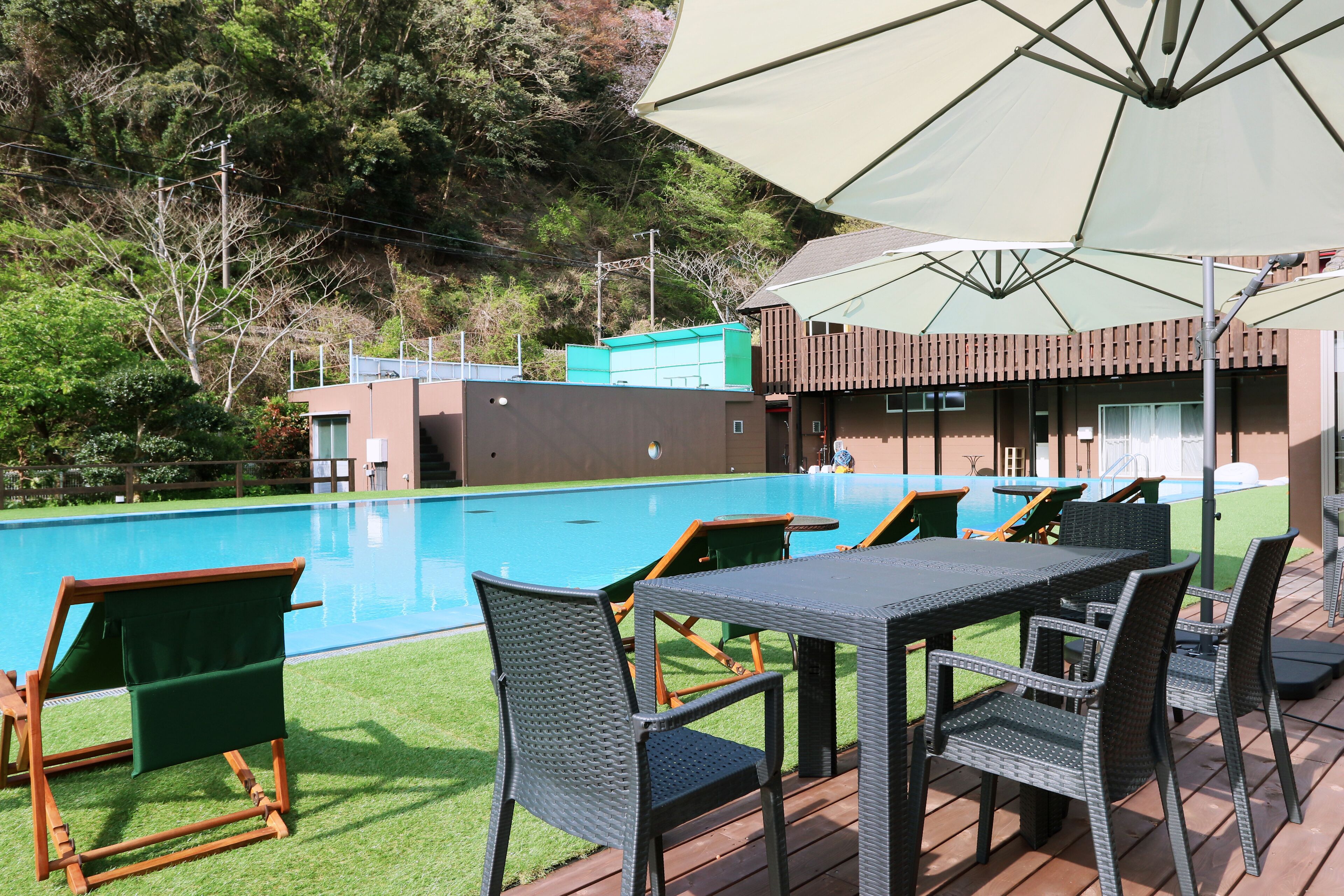 Un área junto a la piscina con mobiliario exterior, una mesa y una sombrilla grande.