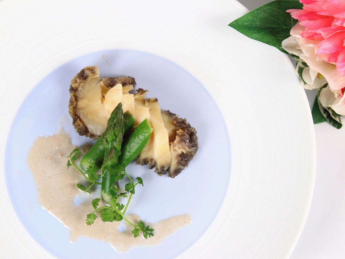 A plate with a food item, possibly a mushroom, garnished with green herbs and a creamy sauce.