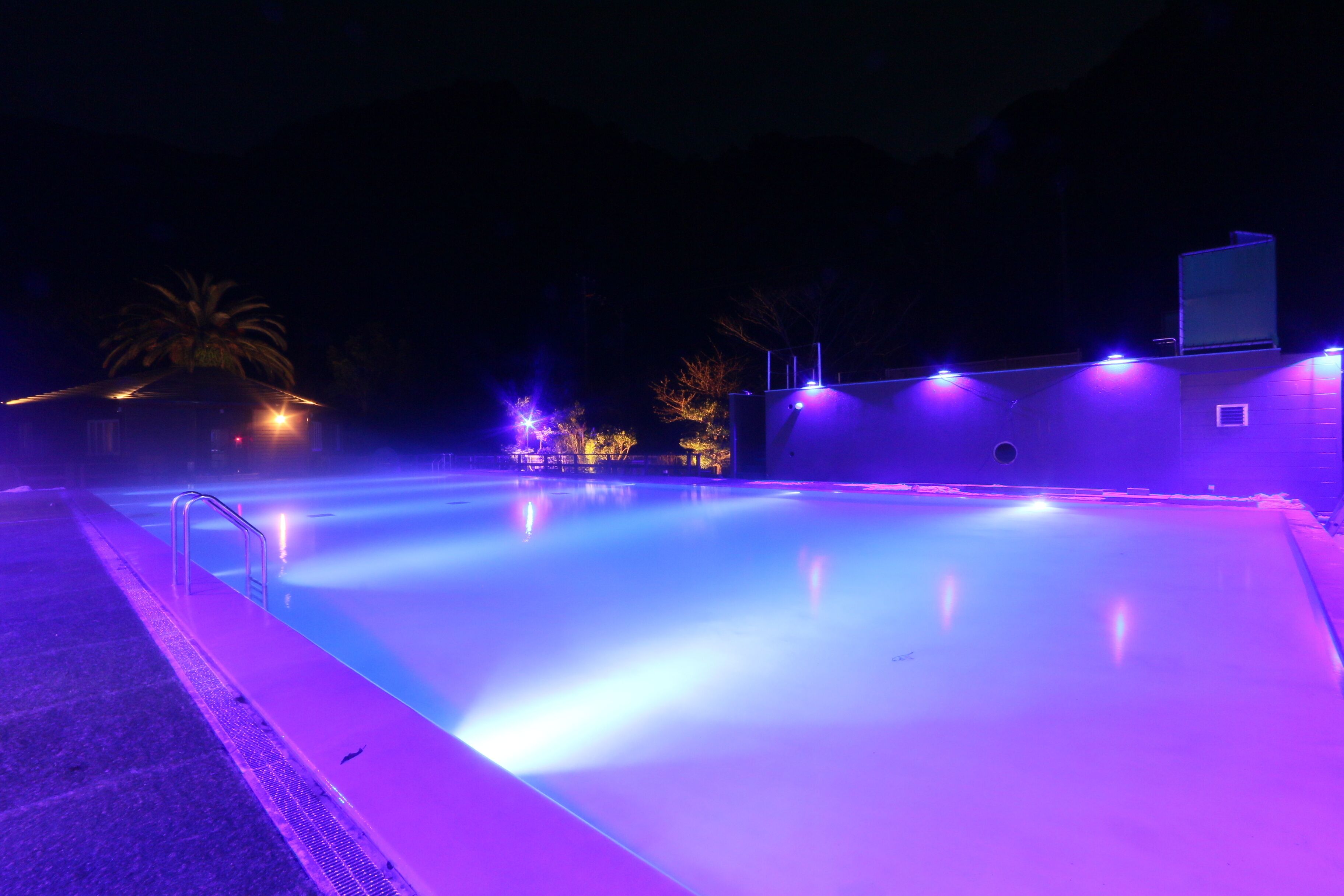 Una piscina exterior iluminada de morado en la noche.