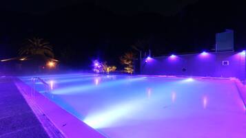 Una piscina exterior iluminada de morado en la noche.