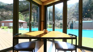 Un comedor con mesa y sillas, ventanas amplias con vistas a una piscina y paisaje circundante.