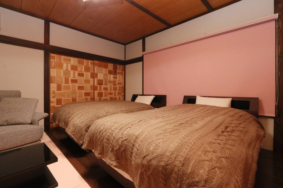 A bedroom with two beds, a chair, and a wooden ceiling.